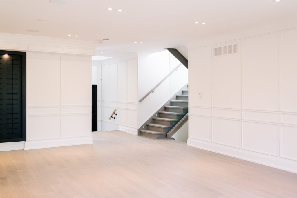 Modern Toronto interior with taupe hardwood flooring, glass railing staircase, and custom wall paneling by Qarnis Development.